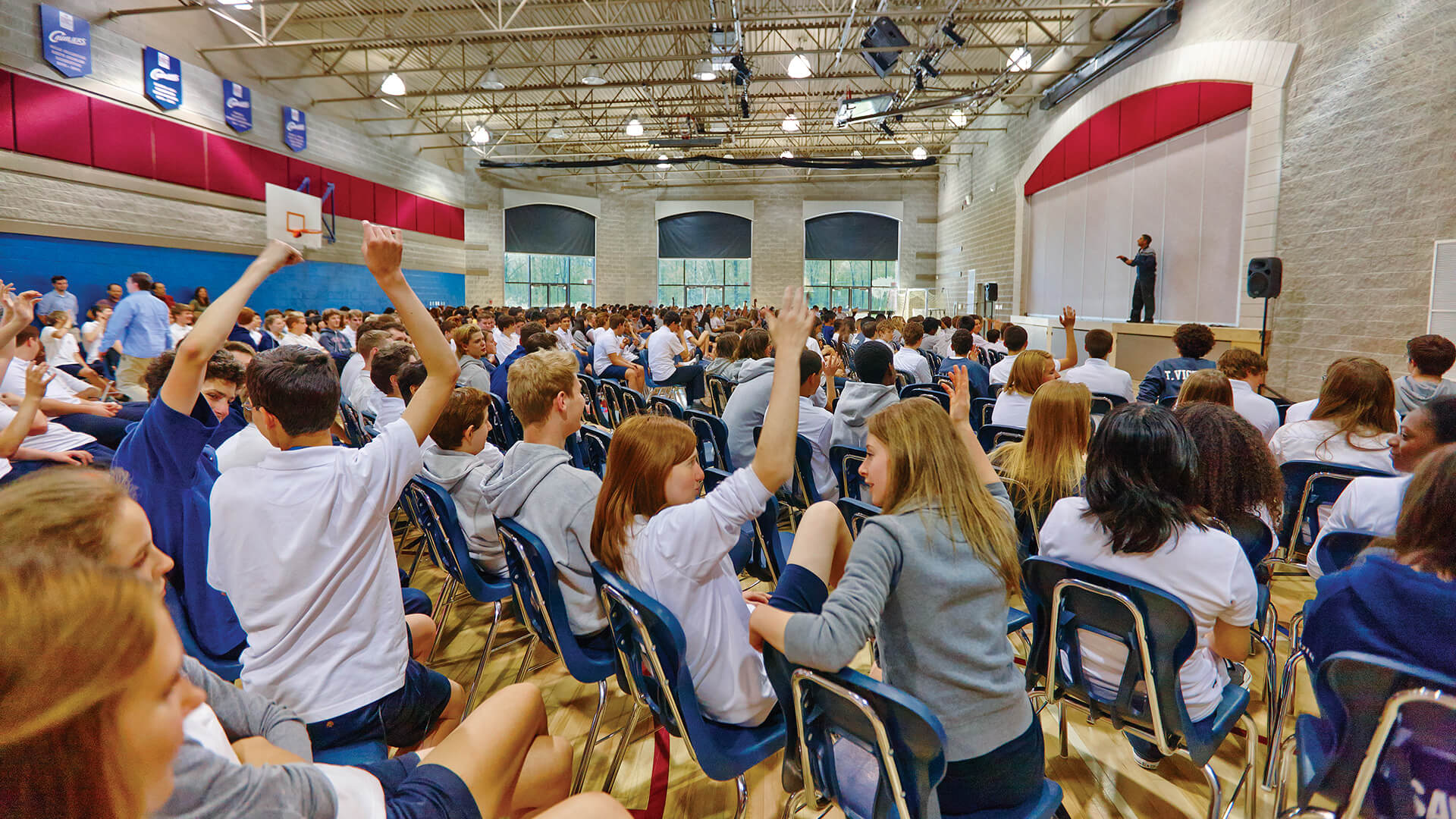 students enthusiastically raising their hands in an assembly